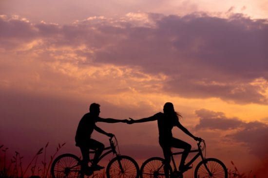 a man and a woman are holding hands while riding bicycles at sunset .