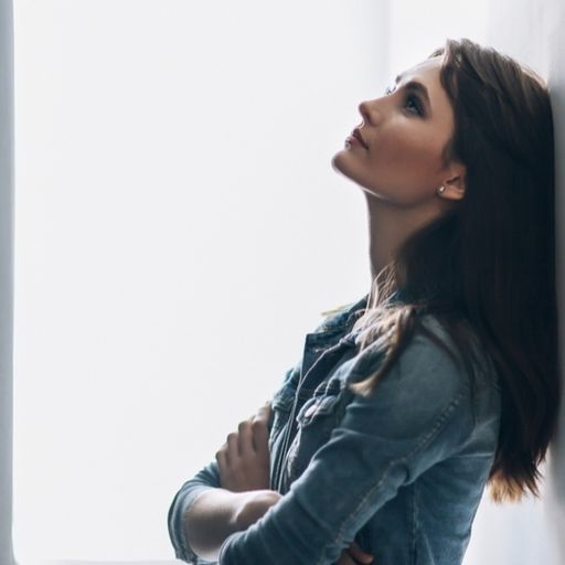 a woman is leaning against a wall while looking out of a window .