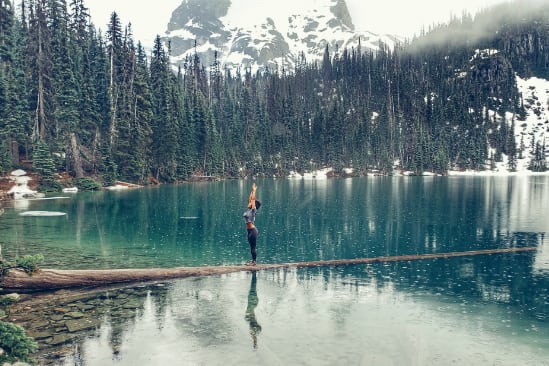 a woman is standing on a log overlooking a lake .