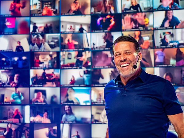 Tony Robbins smiles with a headset in front of a grid of virtual attendees.