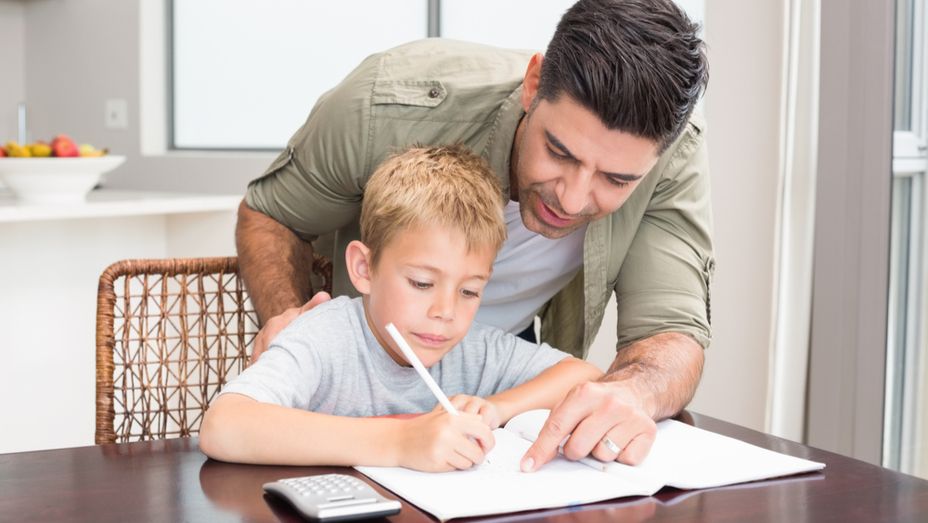 a man is helping a young boy with his homework at a table .
