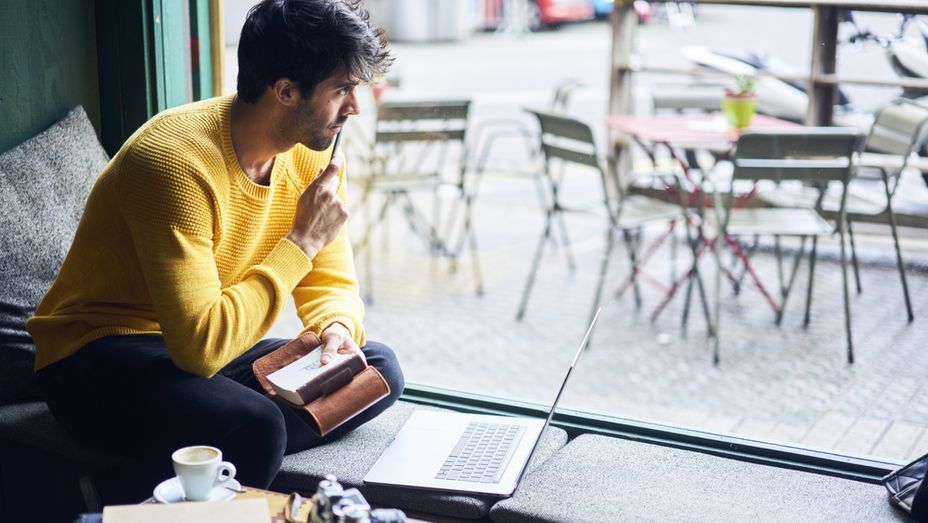 a man in a yellow sweater is sitting in front of a window with a laptop .