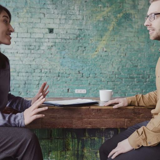 a man and a woman are sitting at a table having a conversation .