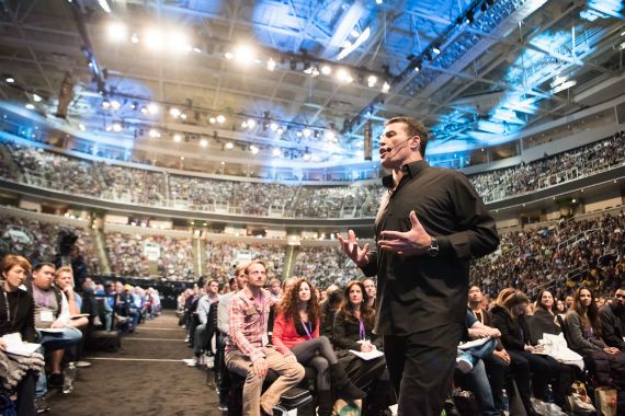 a man is giving a speech in front of a crowd in a stadium .
