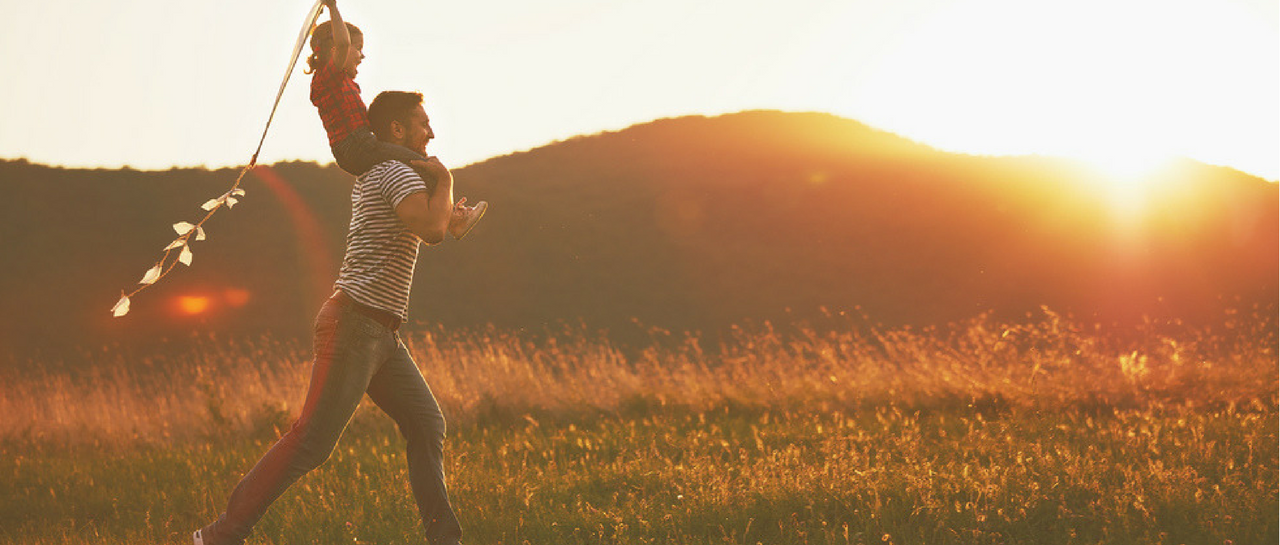 a man is carrying a child on his shoulders in a field at sunset