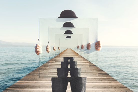 a person is holding a mirror with a reflection of a person standing on a pier .