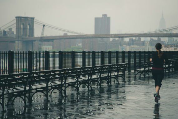 a woman is running in the rain near a bridge .