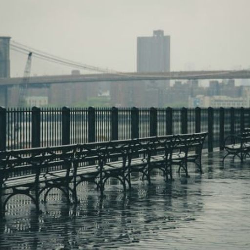 a woman is running in the rain near a bridge .