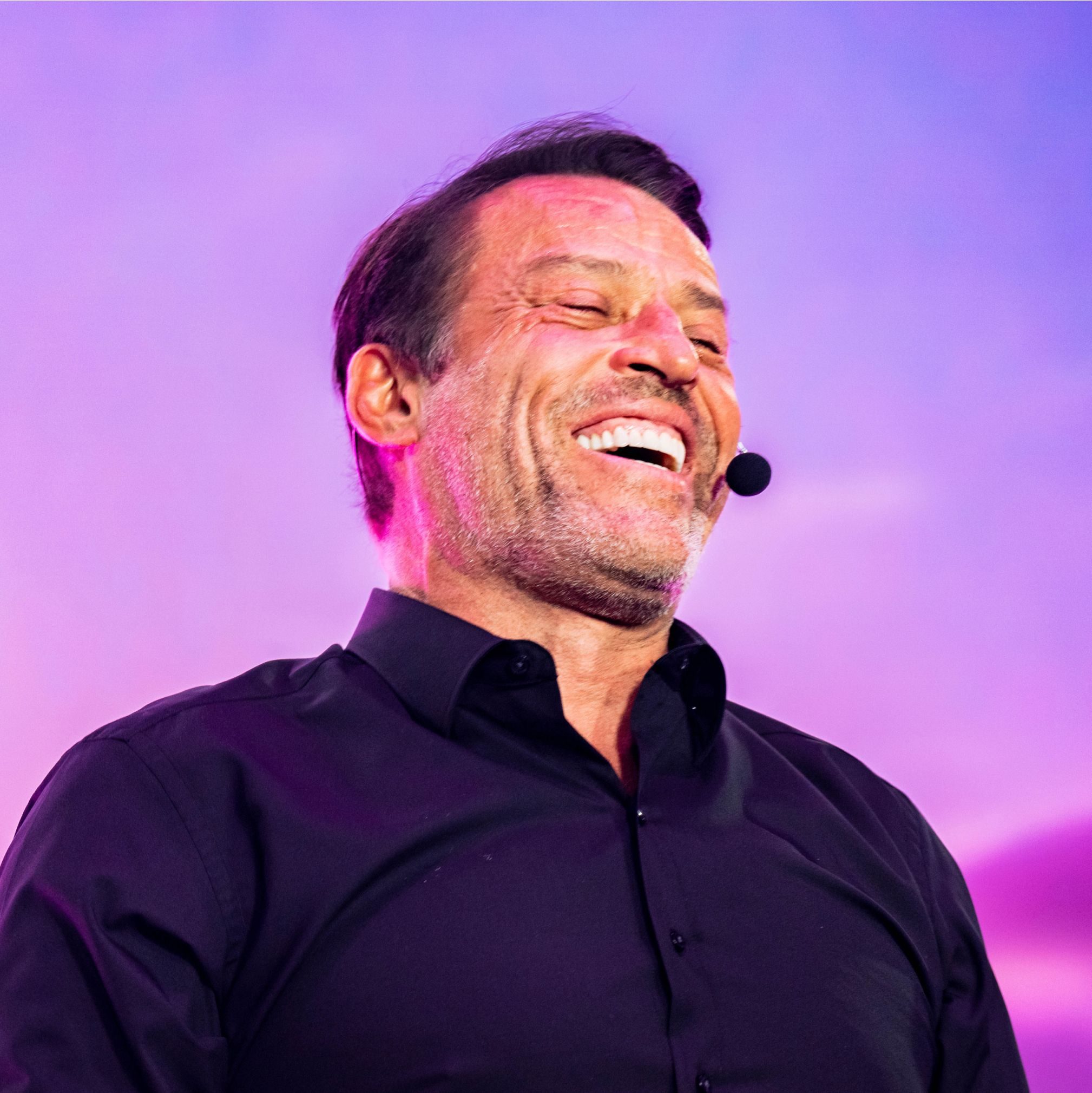 a man in a black shirt is laughing into a microphone .