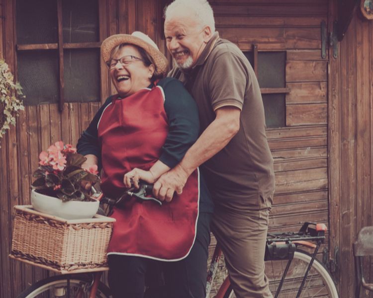 an elderly couple is riding a bicycle in front of a wooden building .