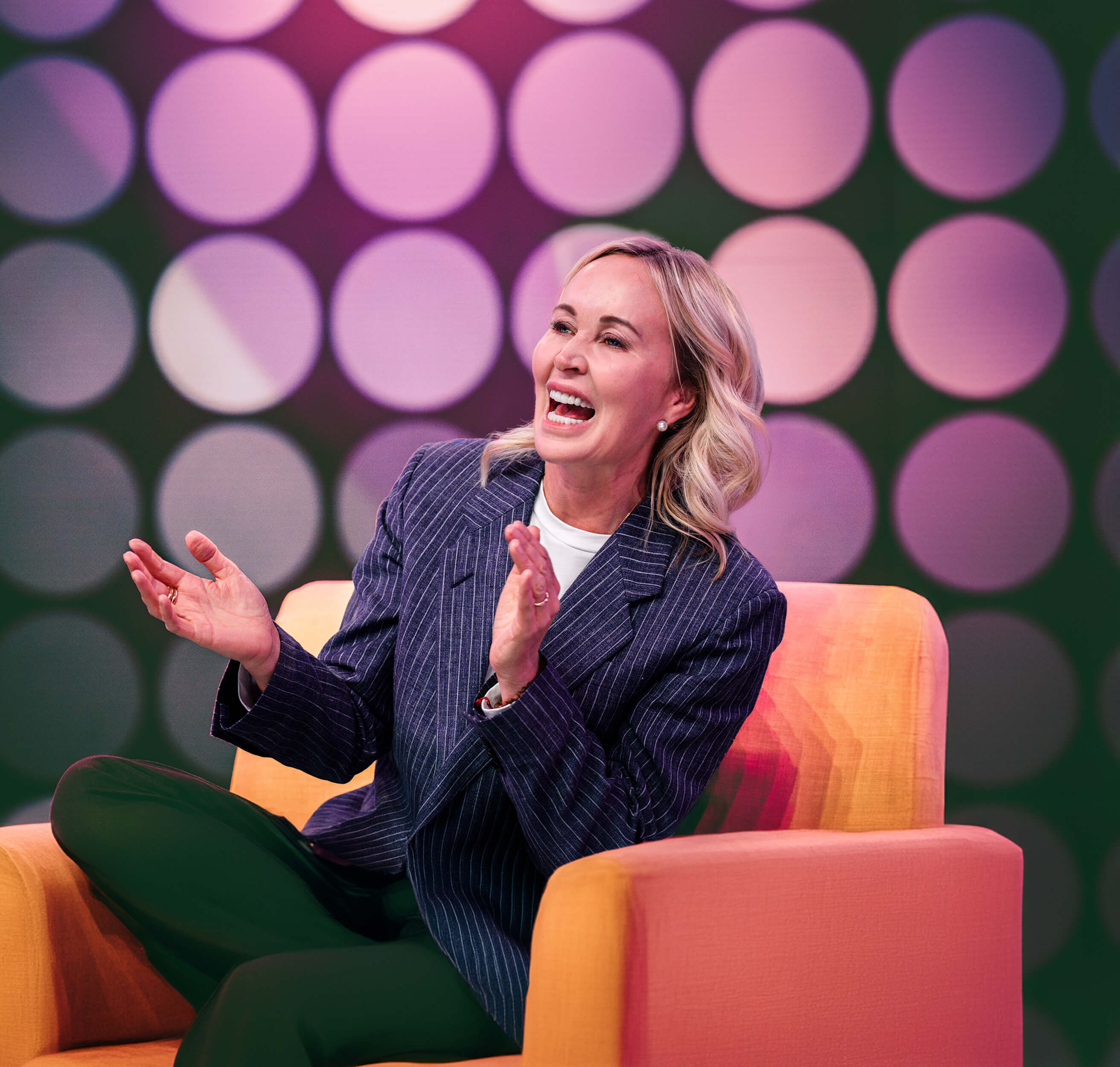 a woman is sitting in a chair laughing and clapping her hands 
