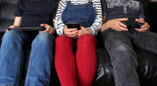 three children are sitting on a couch playing video games .