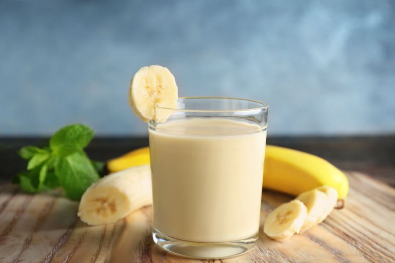 a glass of banana milk with a slice of banana on a wooden table .