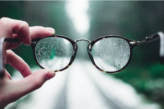 a person is holding a pair of glasses with water drops on them .