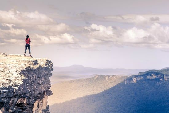 a woman is standing on the edge of a cliff overlooking a mountain range .