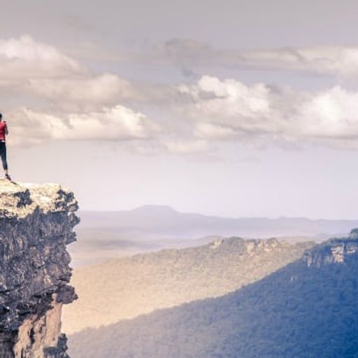 a woman is standing on the edge of a cliff overlooking a mountain range .