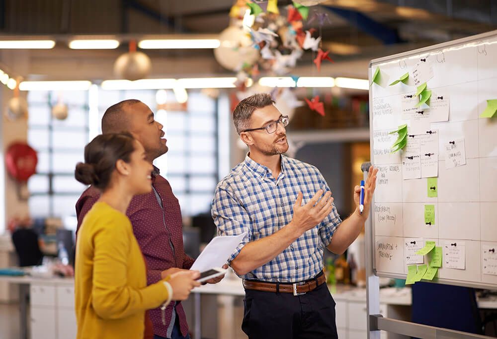 a group of people are standing around a whiteboard in an office .