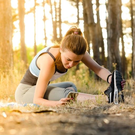 a woman is sitting on a yoga mat in the woods stretching her legs .