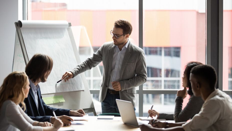 a man is giving a presentation to a group of people sitting around a table .
