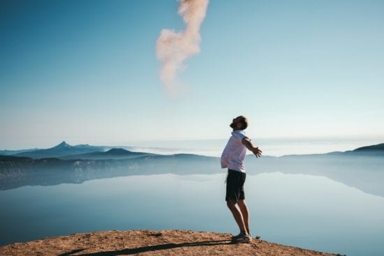 a man is standing on top of a hill overlooking a lake with his arms outstretched .