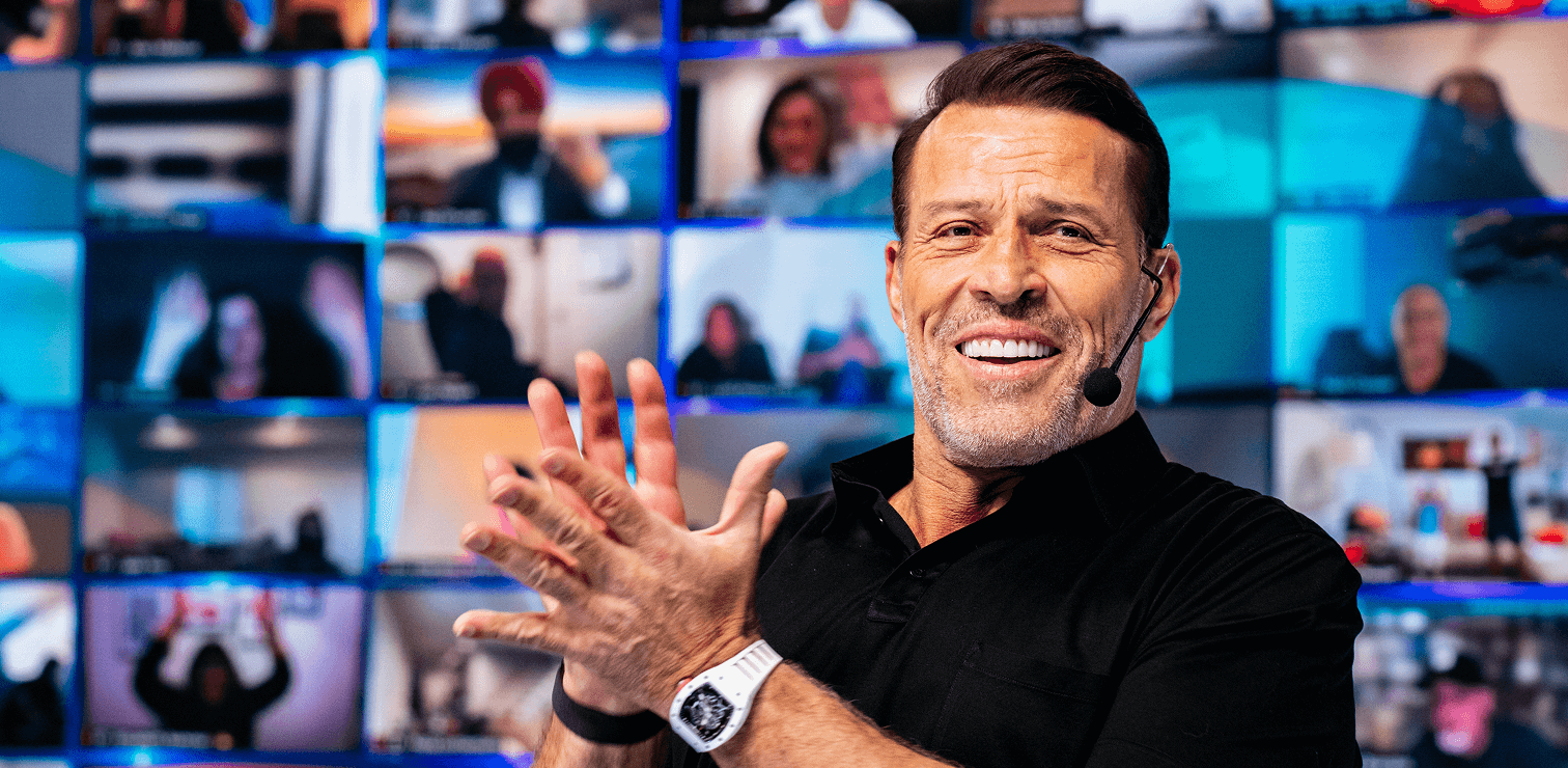a man wearing a microphone applauds in front of a wall of screens