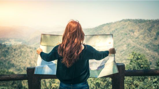 a woman is looking at a map on top of a mountain .