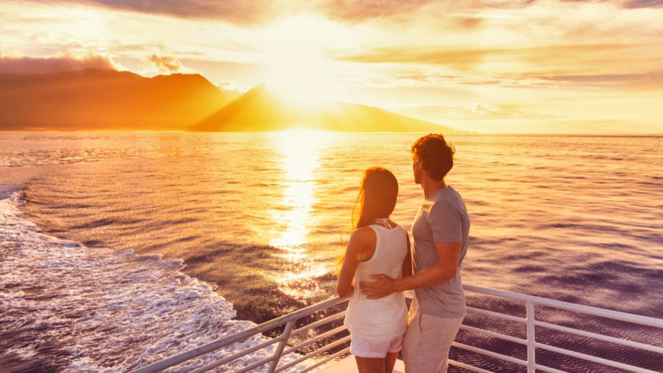 a man and a woman are standing on a boat looking at the sunset .