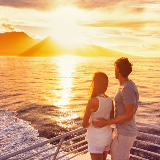 a man and a woman are standing on a boat looking at the sunset .