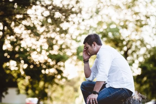 a man is sitting on a rock in a park with his head in his hands .