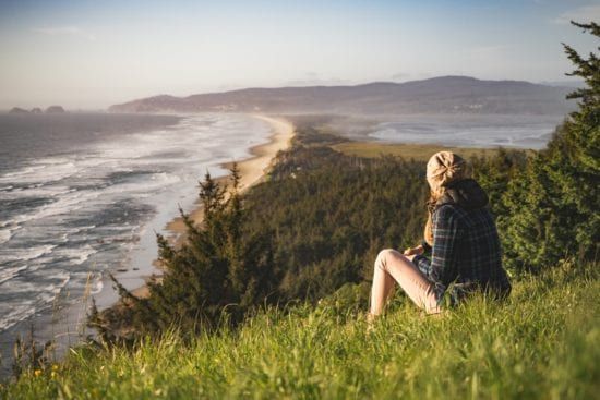 a woman is sitting on top of a grassy hill overlooking the ocean .