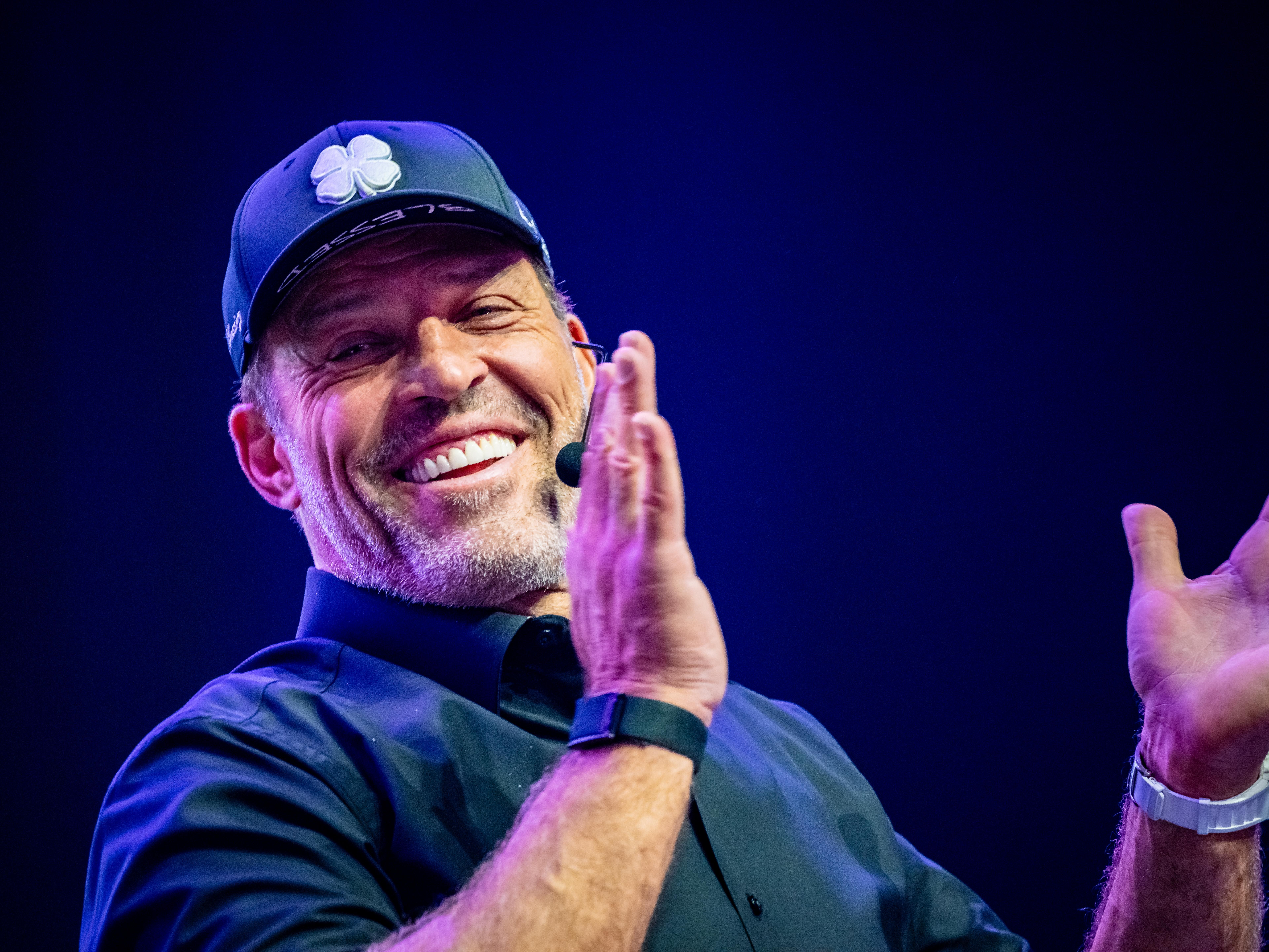 a man wearing a hat and a watch is smiling and clapping his hands .