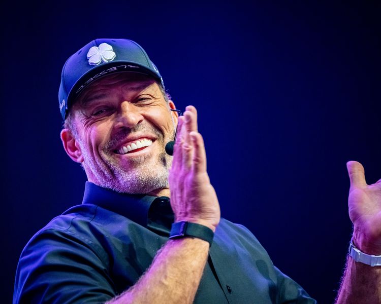 a man wearing a hat and a watch is smiling and clapping his hands .