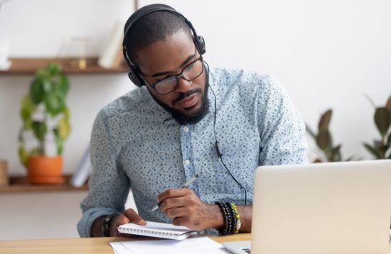 a man wearing headphones is sitting at a desk in front of a laptop computer .