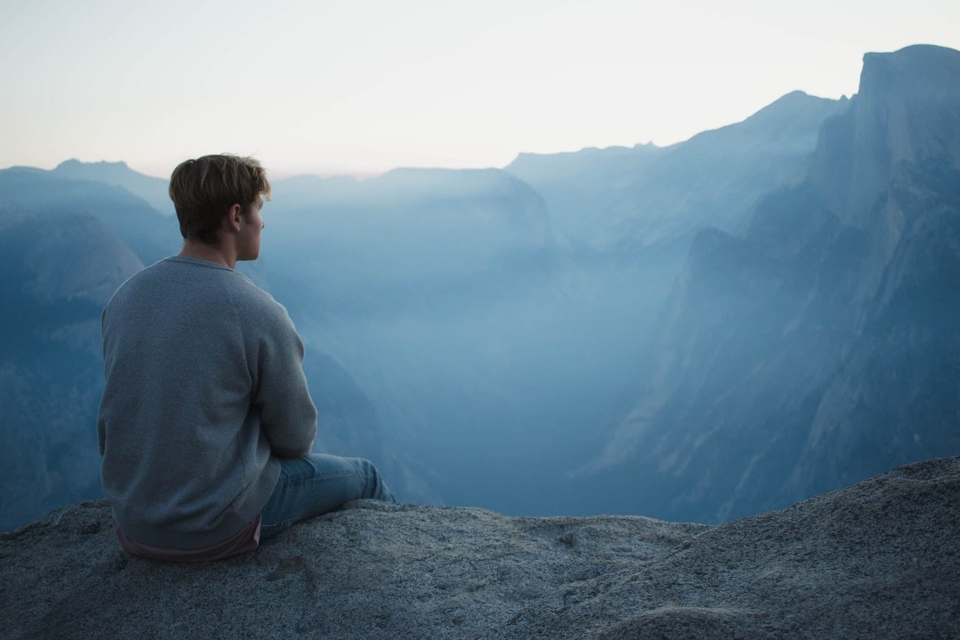 a man is sitting on top of a rock overlooking a mountain range .