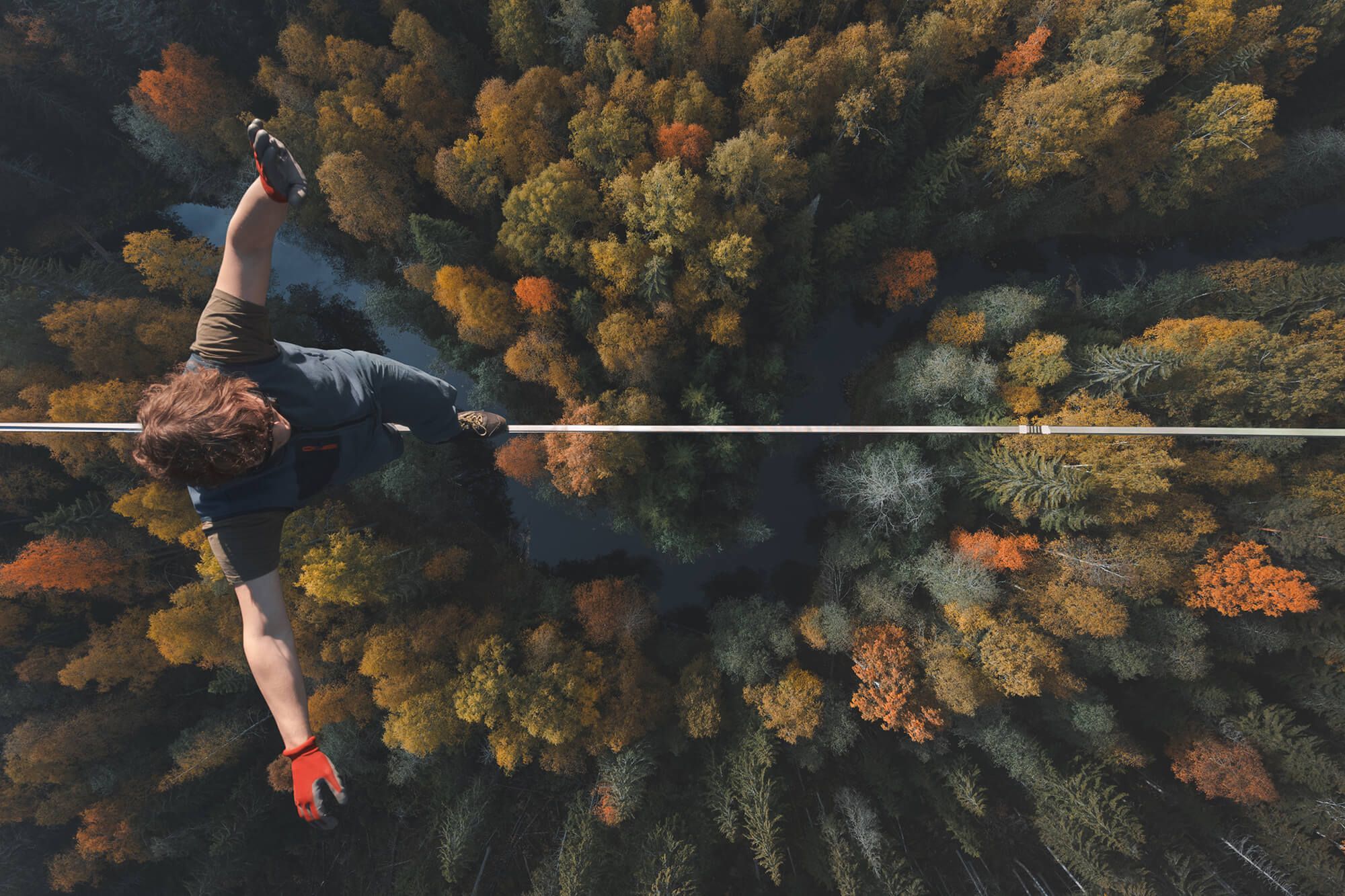 Overhead view of a person slacklining high above an autumn forest.