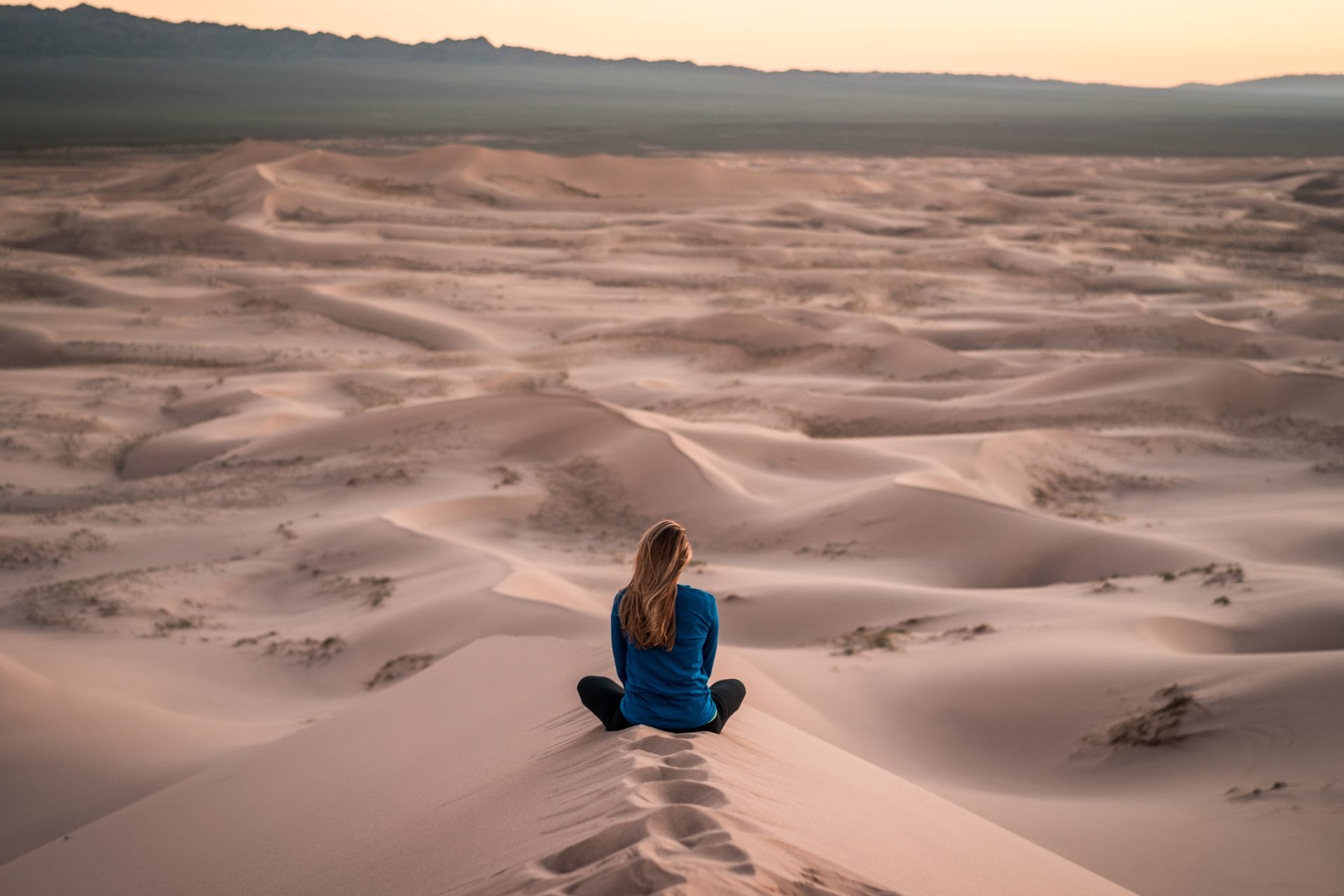 a woman is sitting on top of a sand dune in the desert .