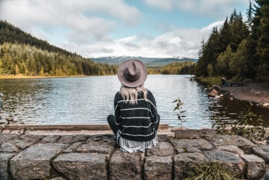 a woman in a hat is sitting on a rock near a lake .