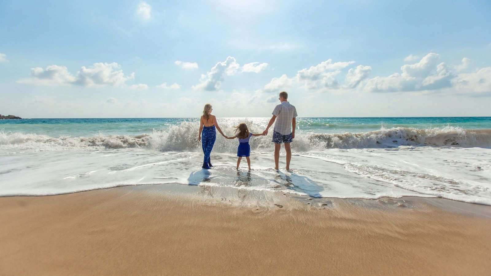 a family is walking on the beach holding hands .