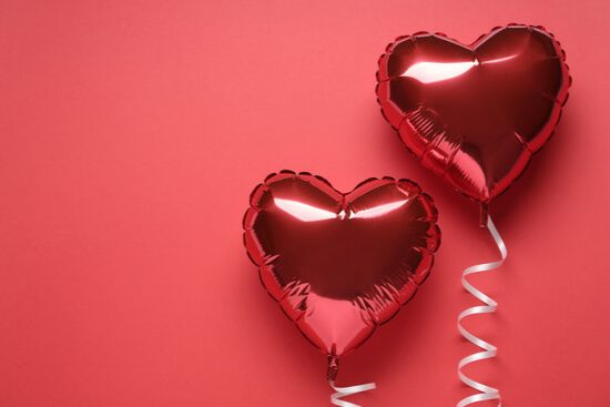 two red heart shaped balloons with a ribbon on a red background .