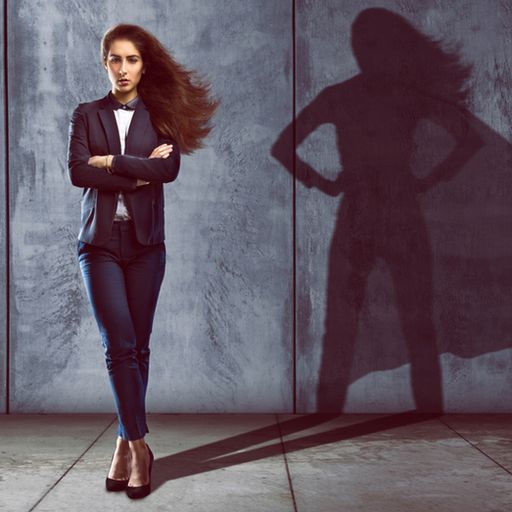 a woman is standing in front of a wall with her shadow of a superhero .