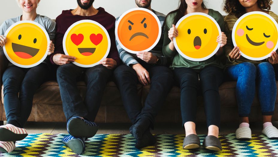 a group of people are sitting on a couch holding signs with smiley faces on them .