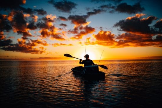 a man is paddling a kayak in the ocean at sunset .