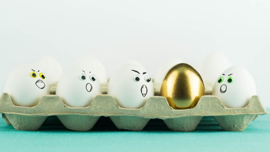 a tray of eggs with faces drawn on them and a gold egg in the middle .