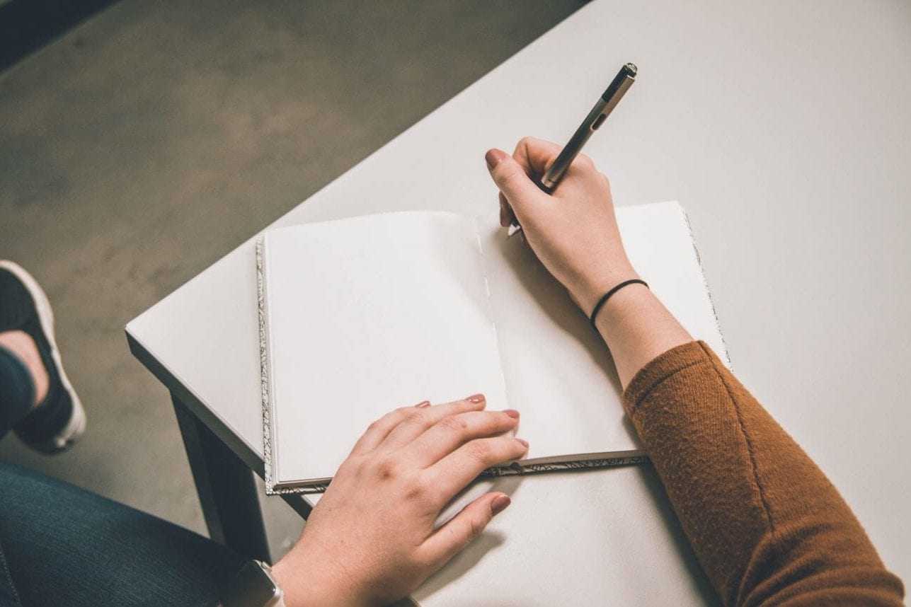 a person is writing in a notebook with a pen .