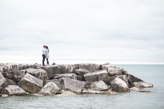 a man and a woman are standing on a rocky pier overlooking the ocean .