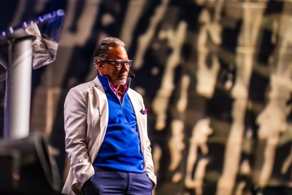 a man in a blue sweater and white jacket is standing in front of a podium .