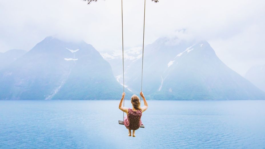 a woman is sitting on a swing overlooking a lake .