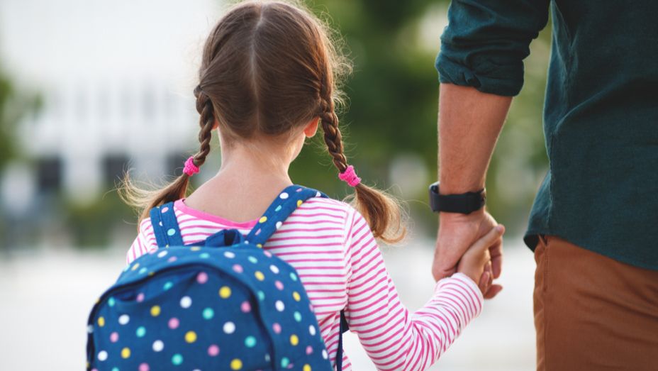 a little girl with a backpack is holding a man 's hand .