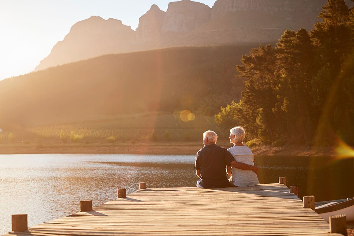 an elderly couple is sitting on a dock overlooking a lake .