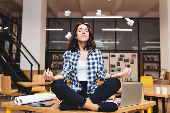a woman is sitting in a lotus position at a desk with a laptop .